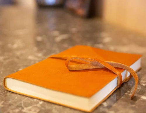 Carnet en cuir orange avec lien, posé sur une table en pierre sombre.Les gîtes du haut bois 2 Le Haut Bois, 25650 Ville-du-Pont, France