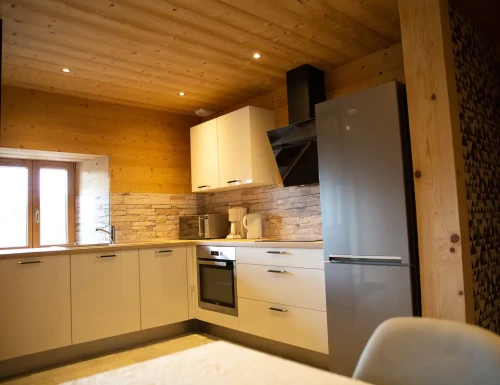 Cuisine équipée moderne avec meubles blancs, réfrigérateur inox et plafond en bois.Les gîtes du haut bois 2 Le Haut Bois, 25650 Ville-du-Pont, France