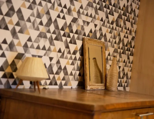 Décoration intérieure avec mur géométrique noir et beige, miroir et objets en rotin sur une commode.Les gîtes du haut bois 2 Le Haut Bois, 25650 Ville-du-Pont, France