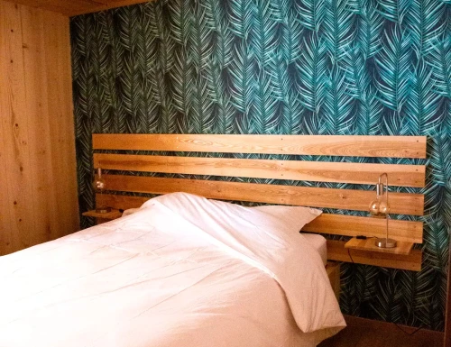 Chambre chaleureuse avec lit en bois et papier peint tropical à motifs de feuilles vertes.Les gîtes du haut bois 2 Le Haut Bois, 25650 Ville-du-Pont, France