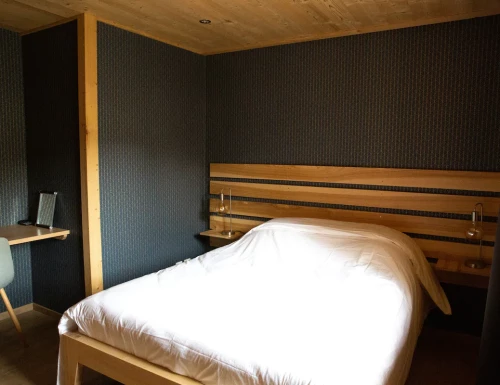 Chambre cosy avec lit double en bois et mur sombre texturé.Les gîtes du haut bois 2 Le Haut Bois, 25650 Ville-du-Pont, France
