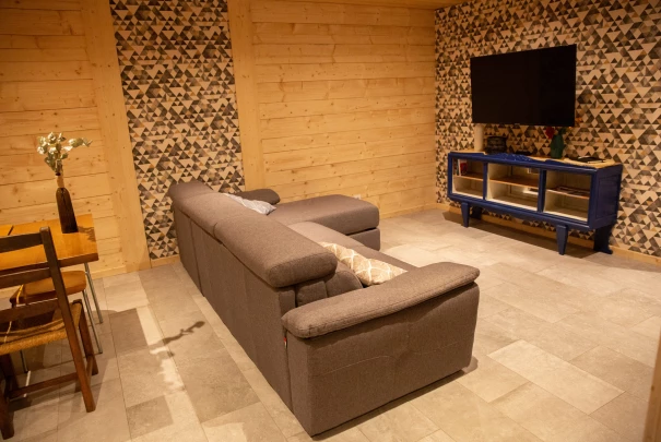 Espace salon avec canapé gris et meuble TV bleu, murs en bois et décoration murale texturée.Les gîtes du haut bois 2 Le Haut Bois, 25650 Ville-du-Pont, France