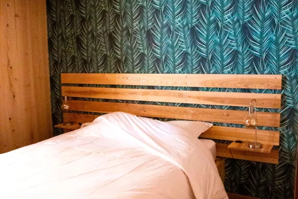 Chambre avec lit double en bois et papier peint bleu-vert à motif de feuilles tropicales.Les gîtes du haut bois 2 Le Haut Bois, 25650 Ville-du-Pont, France