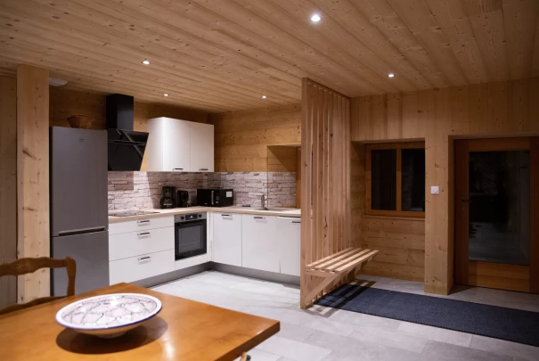 Cuisine moderne en bois éclairée de nuit, avec banc en bois et meubles clairs.Les gîtes du haut bois 2 Le Haut Bois, 25650 Ville-du-Pont, France