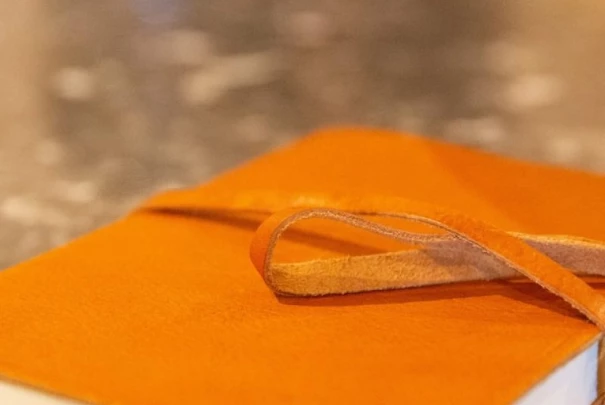 Carnet en cuir orange posé sur une surface en pierre avec un ruban de fermeture Les gîtes du haut bois 2 Le Haut Bois, 25650 Ville-du-Pont, France